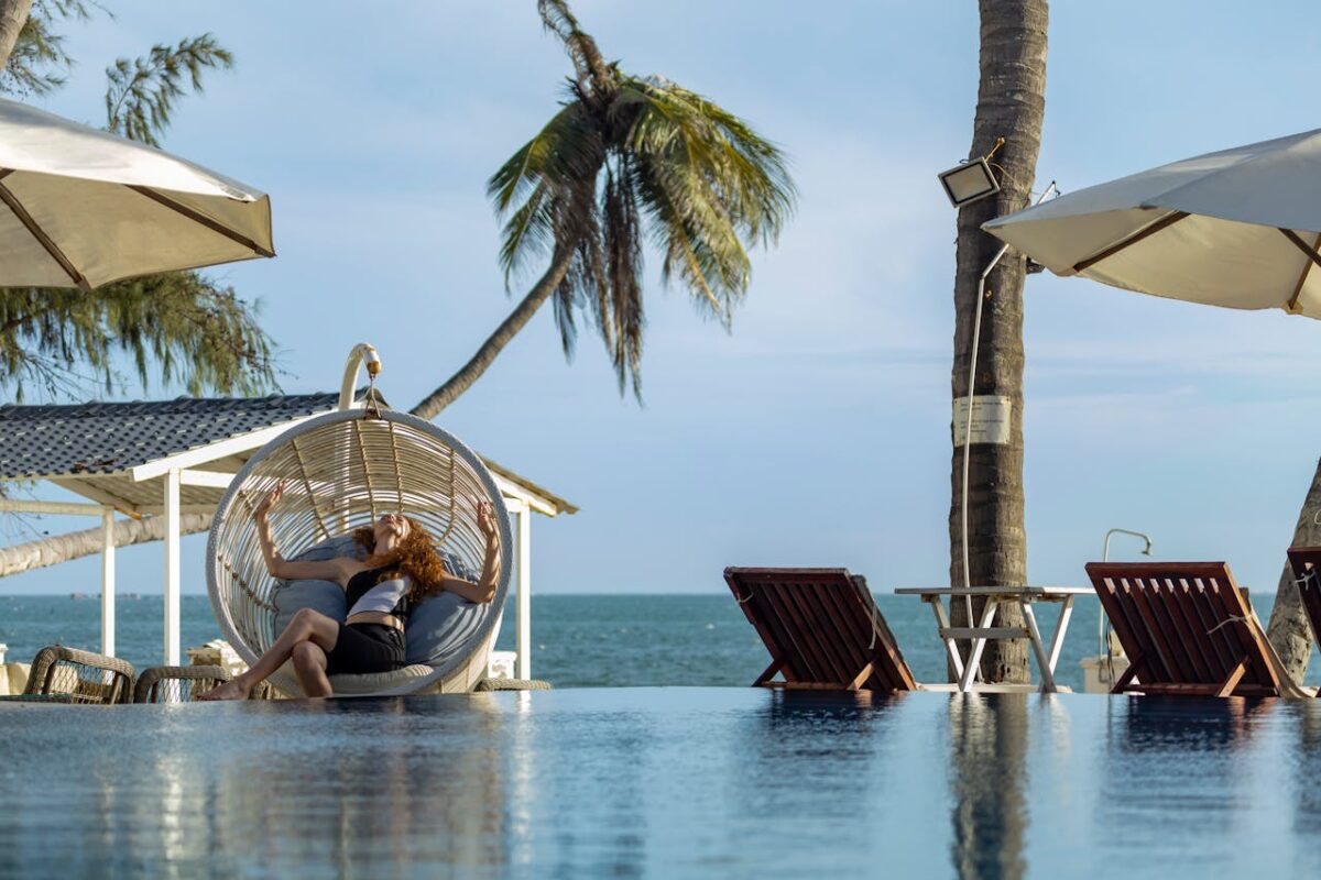 Woman lounging in a hammock chair by the pool with ocean view, perfect for a relaxing vacation.