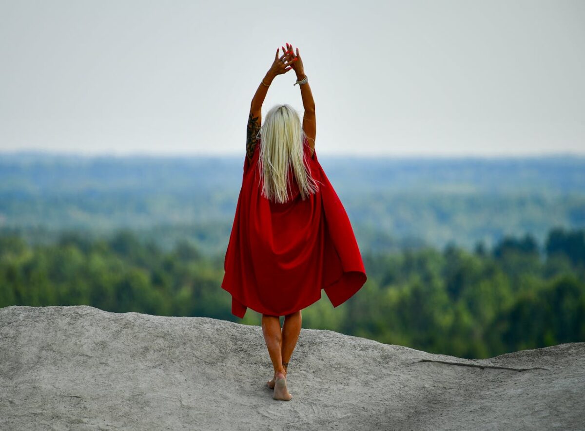 A woman in a red cloak stands gracefully on a cliff, embracing nature in Vasalemma, Estonia.