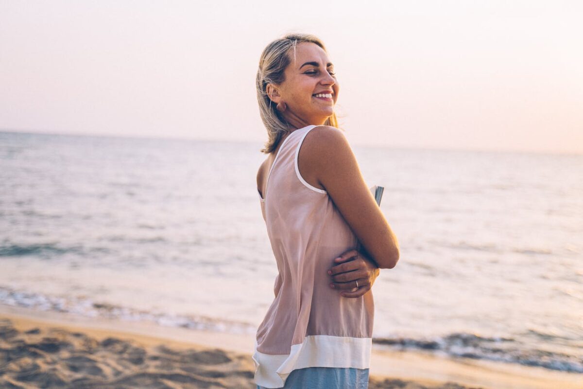 Happy woman holding a notebook, smiling on a serene beach at sunset.