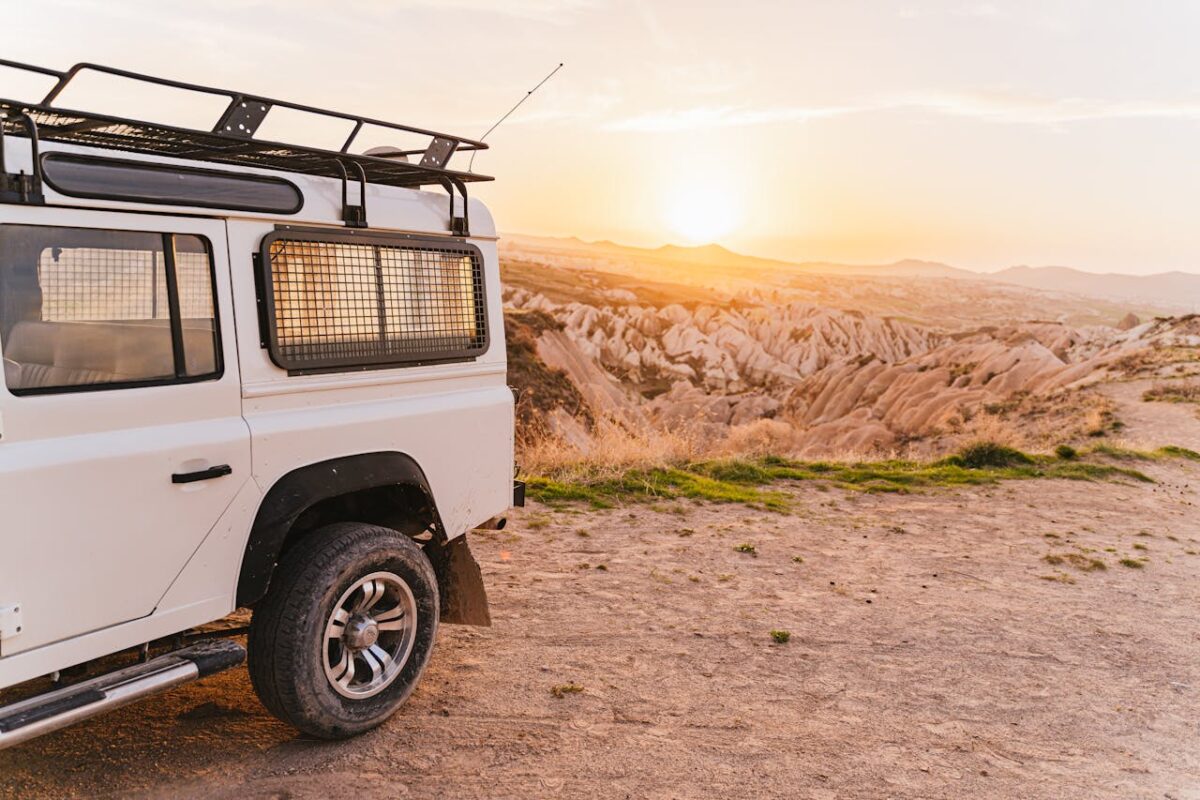 An off-road vehicle parked on a dirt road, overlooking a picturesque desert landscape at sunset.